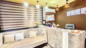A reception area with a sofa, a reception desk, and a wall-mounted air conditioning unit. - Premium Hotel M Shri near Mahakal Temple (Ujjain)