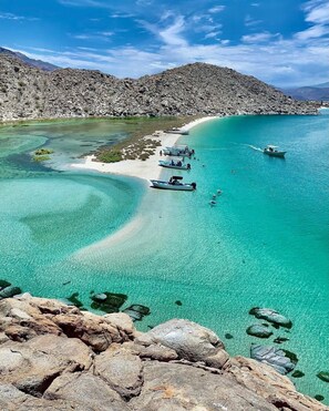 Un paisaje costero con aguas turquesas cristalinas, terreno rocoso y barcos anclados cerca de la orilla.