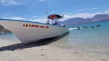 A boat named "La Costa del Sol" docked at a beach with clear water and mountains in the background.