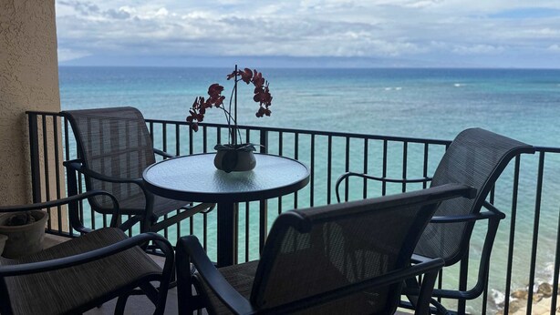 Een balkon met een ronde tafel en twee stoelen, met uitzicht op een strand en de oceaan.
