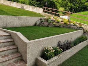 A landscaped garden with stone steps, a grassy area, and a variety of plants.