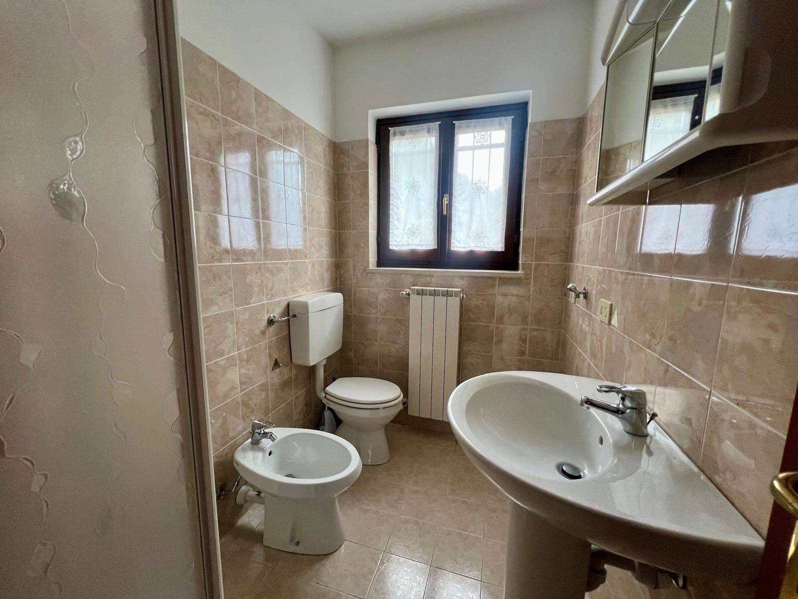 Un baño con baldosas color beige, un inodoro, un bidé y un lavamanos.