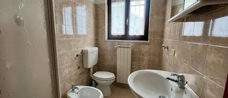 Un baño con baldosas color beige, un inodoro, un bidé y un lavamanos.