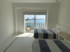 Quarto com uma grande janela com vista para a praia e o horizonte da cidade.