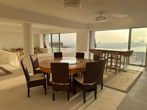 Uma sala de jantar moderna com uma mesa redonda e cadeiras, amplas janelas com vista para a cidade e um teto alto com ventoinha.