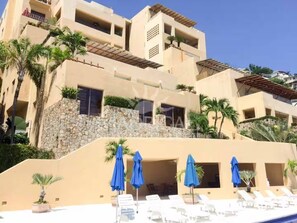 Um hotel com vários andares, área de piscina, espreguiçadeiras e guarda-sóis azuis.