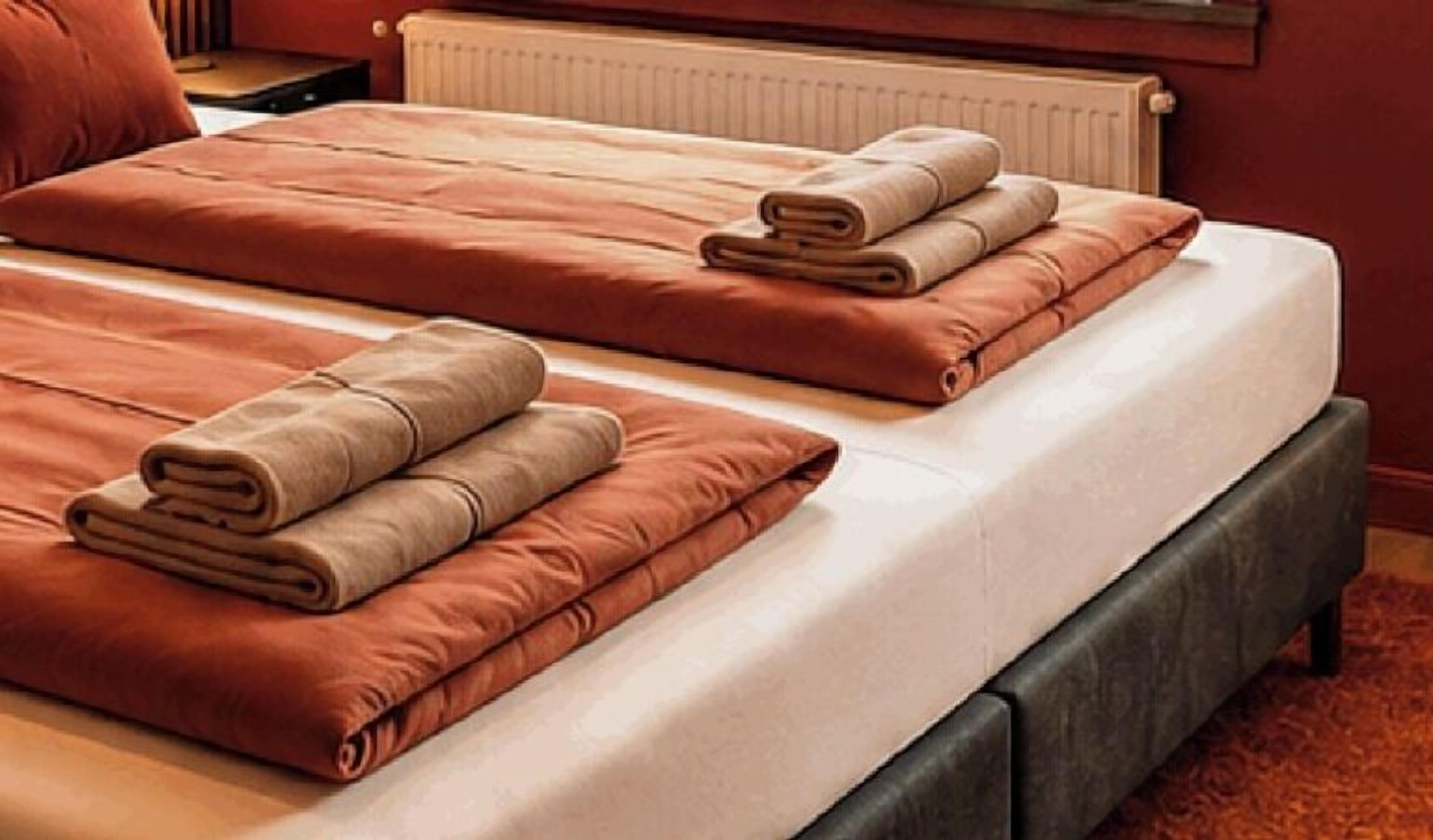 Habitación de hotel con dos camas, cada una con una toalla doblada y un almohadón.
