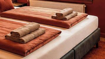 Habitación de hotel con dos camas, cada una con una toalla doblada y un almohadón.