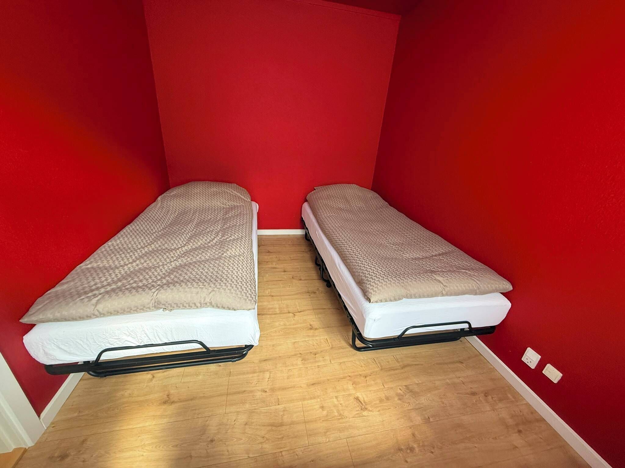 A small room with two single beds against red walls and wooden flooring.