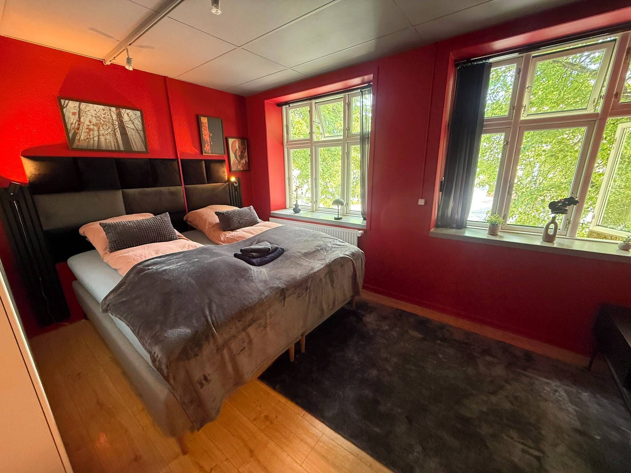Una habitación con cama, ventana y pared roja.