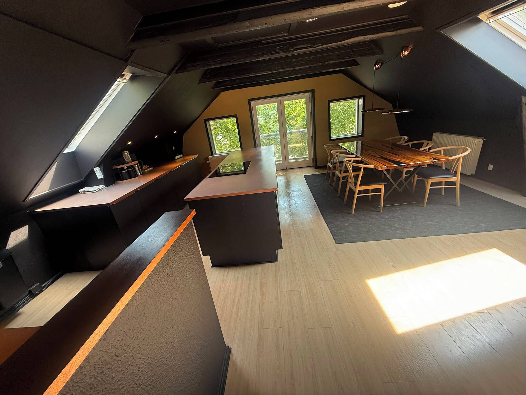 A modern loft with a dining area, kitchen, and large windows.