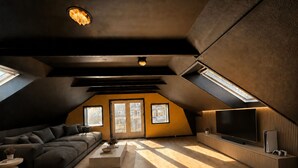 A modern loft-style room with a large sofa, a flat-screen TV, and a wooden floor. - Four Seasons - Crimson Autumn Suite (Aalborg)