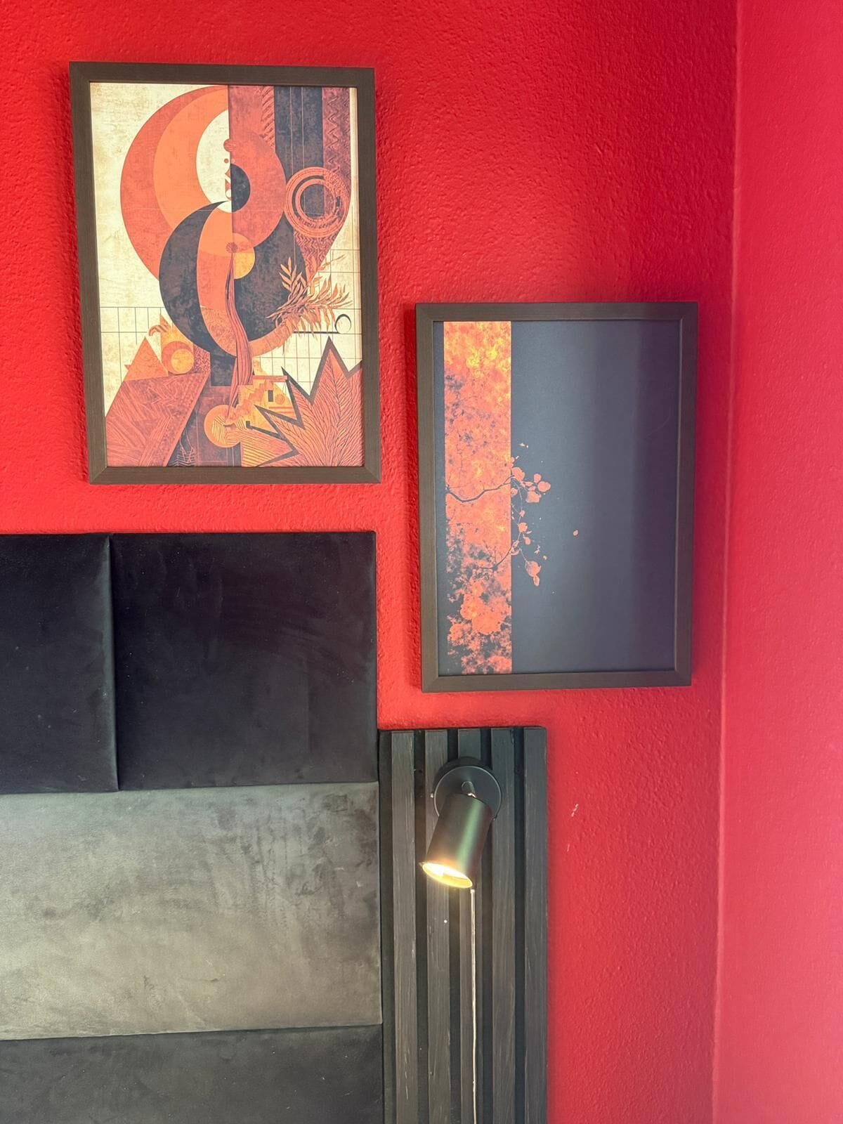 A red wall with two framed artworks and a black headboard.