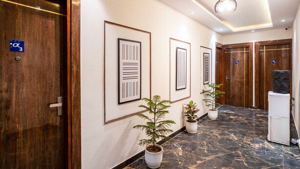 Um corredor com quadros nas paredes, plantas em vasos e uma geladeira.