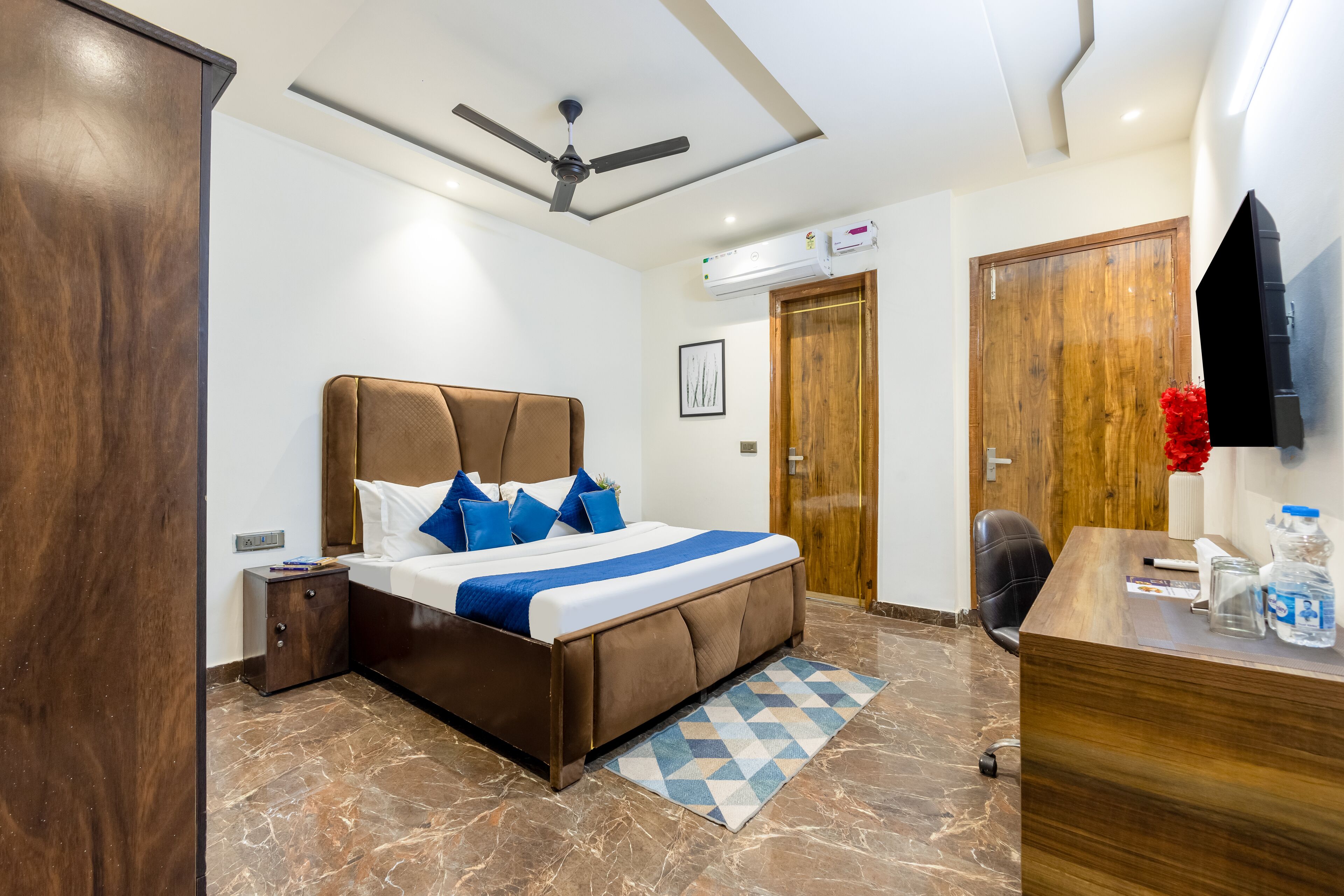 Ein Hotelzimmer mit Bett, Schreibtisch, Stuhl, Deckenventilator und Klimaanlage.