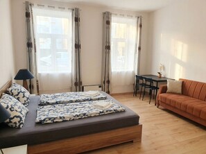 A room with a bed, a sofa, a table, and two windows with curtains. - Only 15 Min to Center - Comfortable 1BR Apartment with TV & WIFI (Vienna)