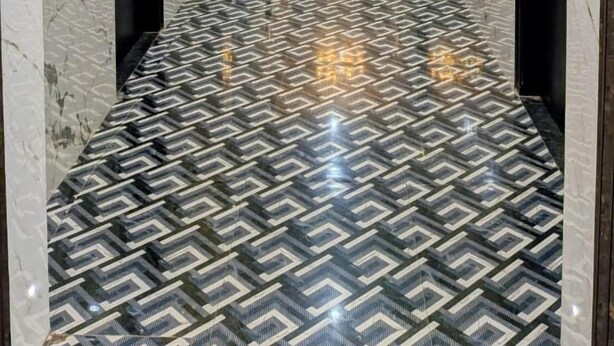 Un couloir doté d’un sol en marbre, d’un lustre et d’un mur orné de motifs.