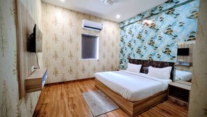 Une chambre avec un plancher en bois, un lit avec une literie blanche, une fenêtre, un climatiseur et un téléviseur fixé au mur.