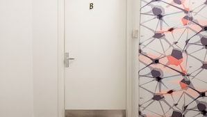 Una porta blanca amb un senyal amb la lletra 'B', un mànec metàl·lic i una paret amb un disseny al costat dret.