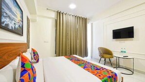 A hotel room with a bed, a chair, a small table, a TV, and curtains. - Hotel Golden Petals (Greater Noida)