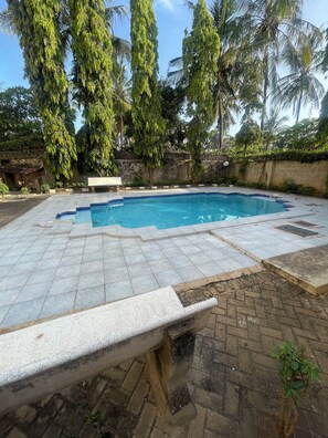 A swimming pool with tiled edges and a brick border, surrounded by palm trees and a stone wall. - Spacious 2BR Apt in Nyali w/Queen Beds & Pool–Great for Groups (Mombasa)