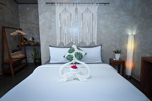 Una cama bien hecha con un colgador de macramé, un perchero de madera y una lámpara de noche.