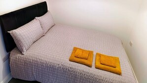 Un lit simple avec une tête de lit noire, une couverture de couleur claire et deux serviettes jaunes pliées posées sur le lit.