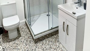 Une salle de bain moderne avec une douche à parois de verre, des toilettes blanches, un lavabo avec un miroir et un meuble de rangement.