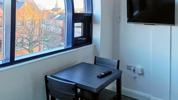 Une pièce dotée d’une fenêtre incurvée, d’un téléviseur à écran plat fixé au mur, d’une table avec une chaise et d’un sol recouvert de moquette.