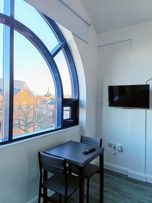 Ein Zimmer mit einem bogenförmigen Fenster, einem an der Wand montierten Flachbildfernseher, einem Tisch mit einem Stuhl und einem Teppichboden.