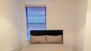 Une chambre à coucher avec un lit, une fenêtre avec des stores et un radiateur.