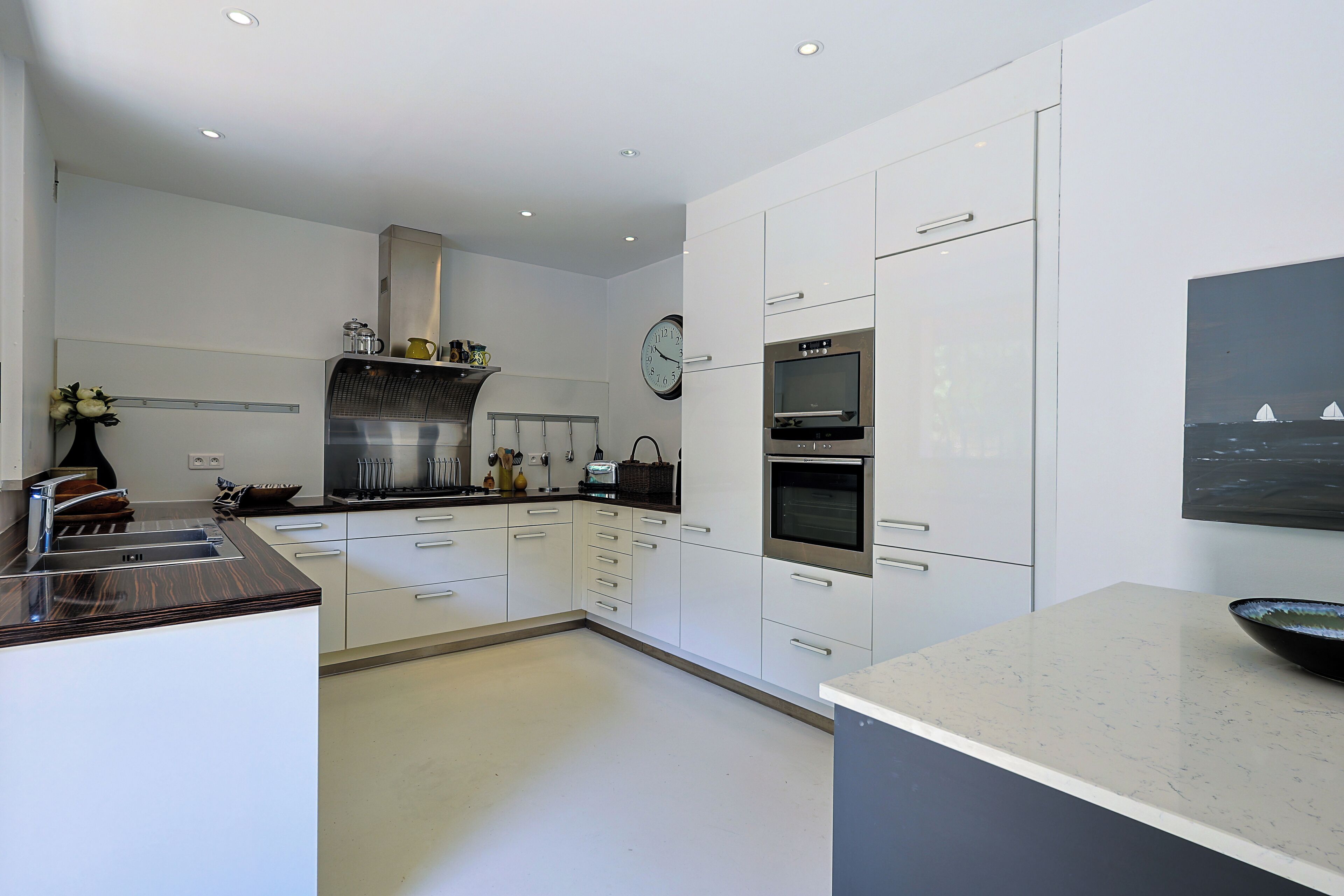 Eine moderne Küche mit weißen Schränken, einem Edelstahlbackofen, einer Mikrowelle und einer Uhr an der Wand.