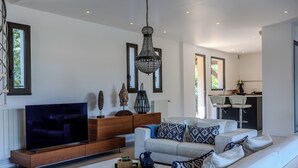 Un salon moderne doté d’un téléviseur à écran plat, de canapés blancs, de coussins à motifs et d’un meuble de rangement en bois.