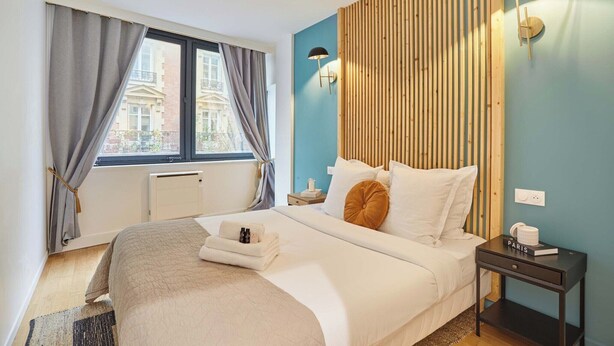 Una camera d'albergo con un letto, un comodino, una lampada e vista sugli edifici.