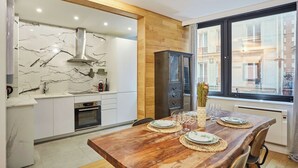 Una cucina moderna con mobili bianchi, zoccolo in marmo e tavolo da pranzo in legno apparecchiato per quattro persone.