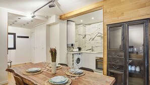 Un'area pranzo con tavolo in legno apparecchiata per quattro persone, una cucina con lavatrice e un armadio con ante in vetro.