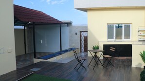 A patio with a wooden table and chairs, a small pool, and a covered area with a red roof.