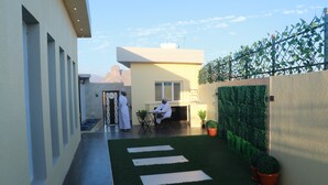 A modern building with a flat roof, a small outdoor seating area with a table and chairs, and a potted plant.