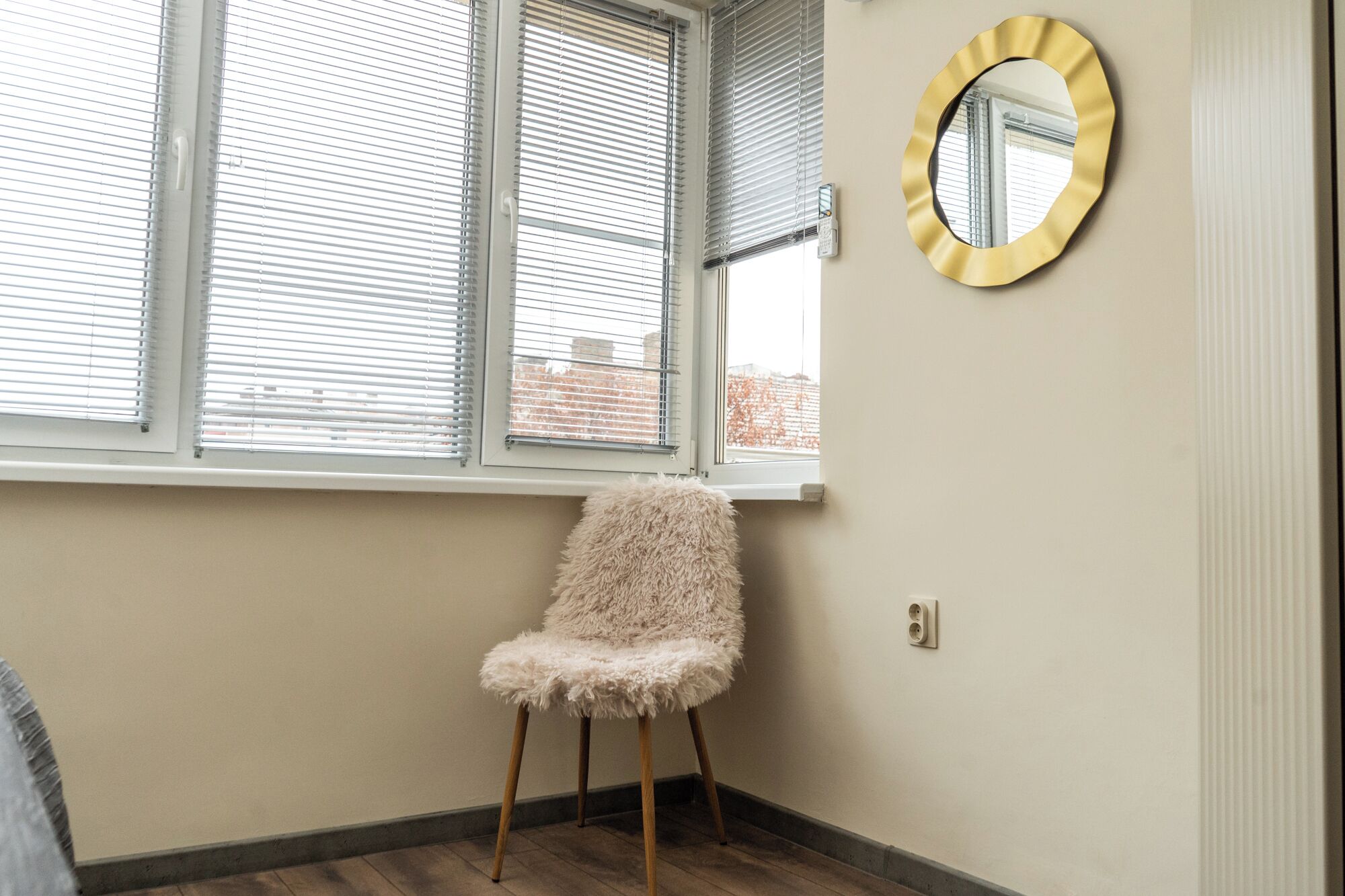 Une pièce avec une fenêtre, un fauteuil moelleux et un miroir rond accroché au mur.