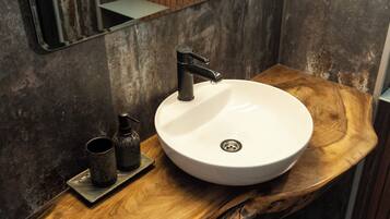 Un baño con un lavabo blanco y redondo, un grifo negro y una pequeña botella de jabón sobre una encimera de madera.