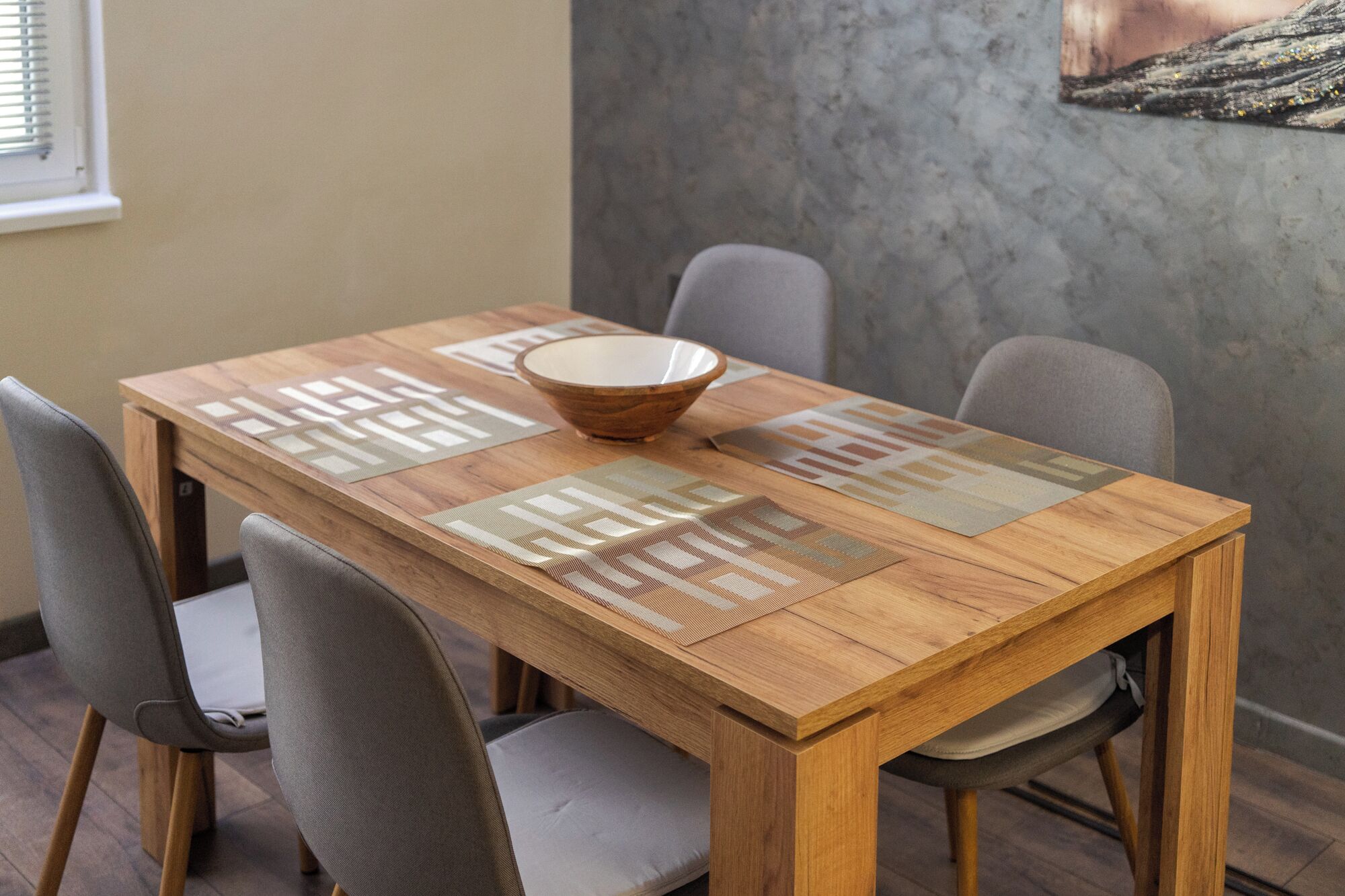 A wooden dining table with a woven placemat, a bowl, and four grey chairs.