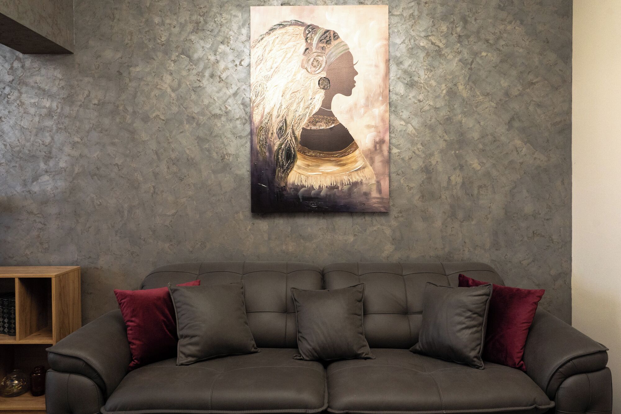 A modern living room with a dark grey sofa, red and black cushions, and a large abstract painting on the wall.