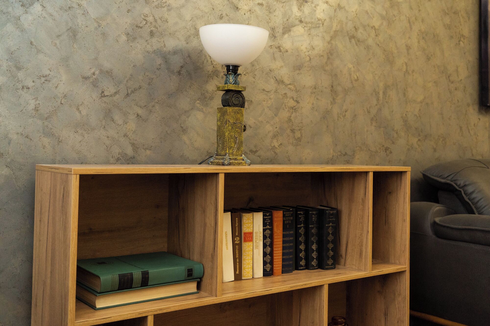 A wooden bookshelf with a white lamp on top, containing several books and a green book on the lower shelf.