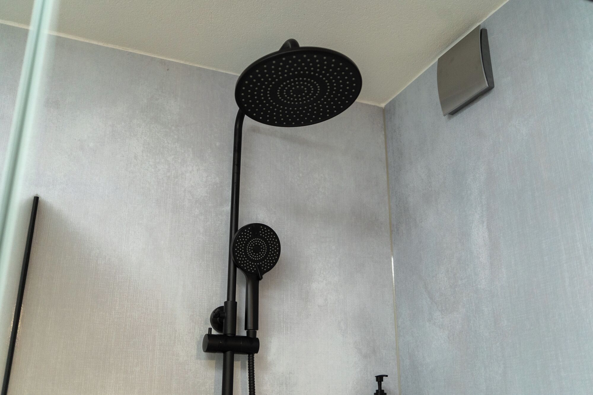 Una ducha con cabezal negro y panel de control.