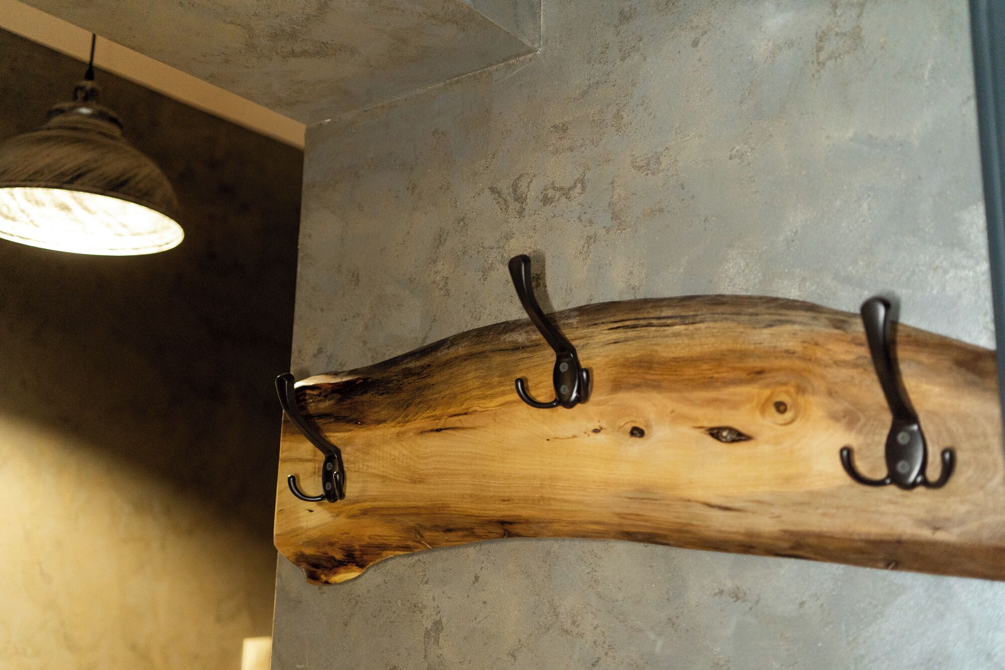A wooden coat rack with hooks against a textured wall.