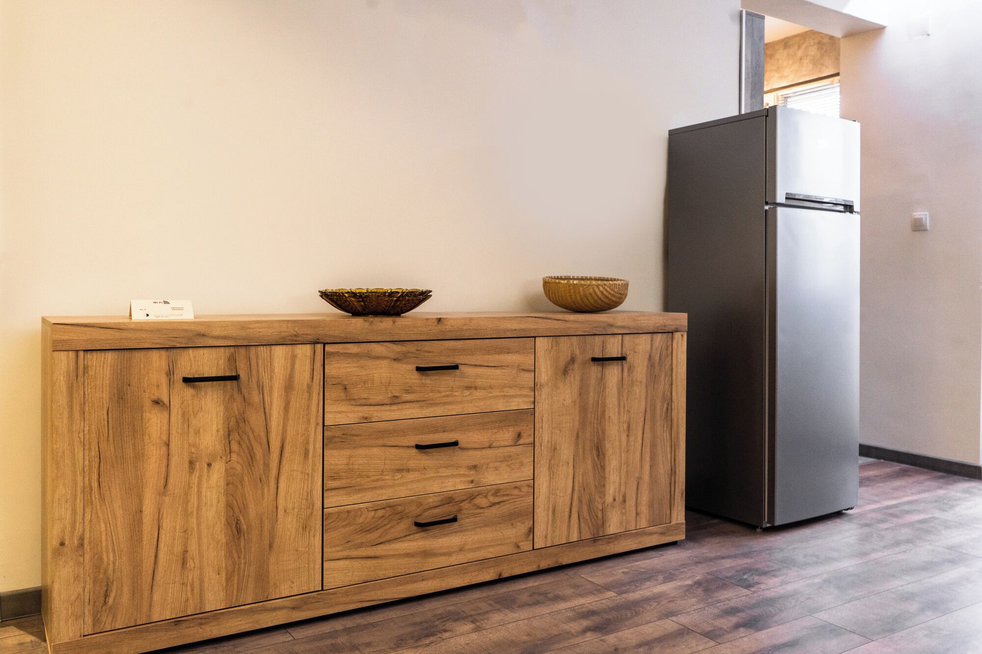A wooden cabinet with drawers and two bowls on top, a black refrigerator, and a wooden floor.