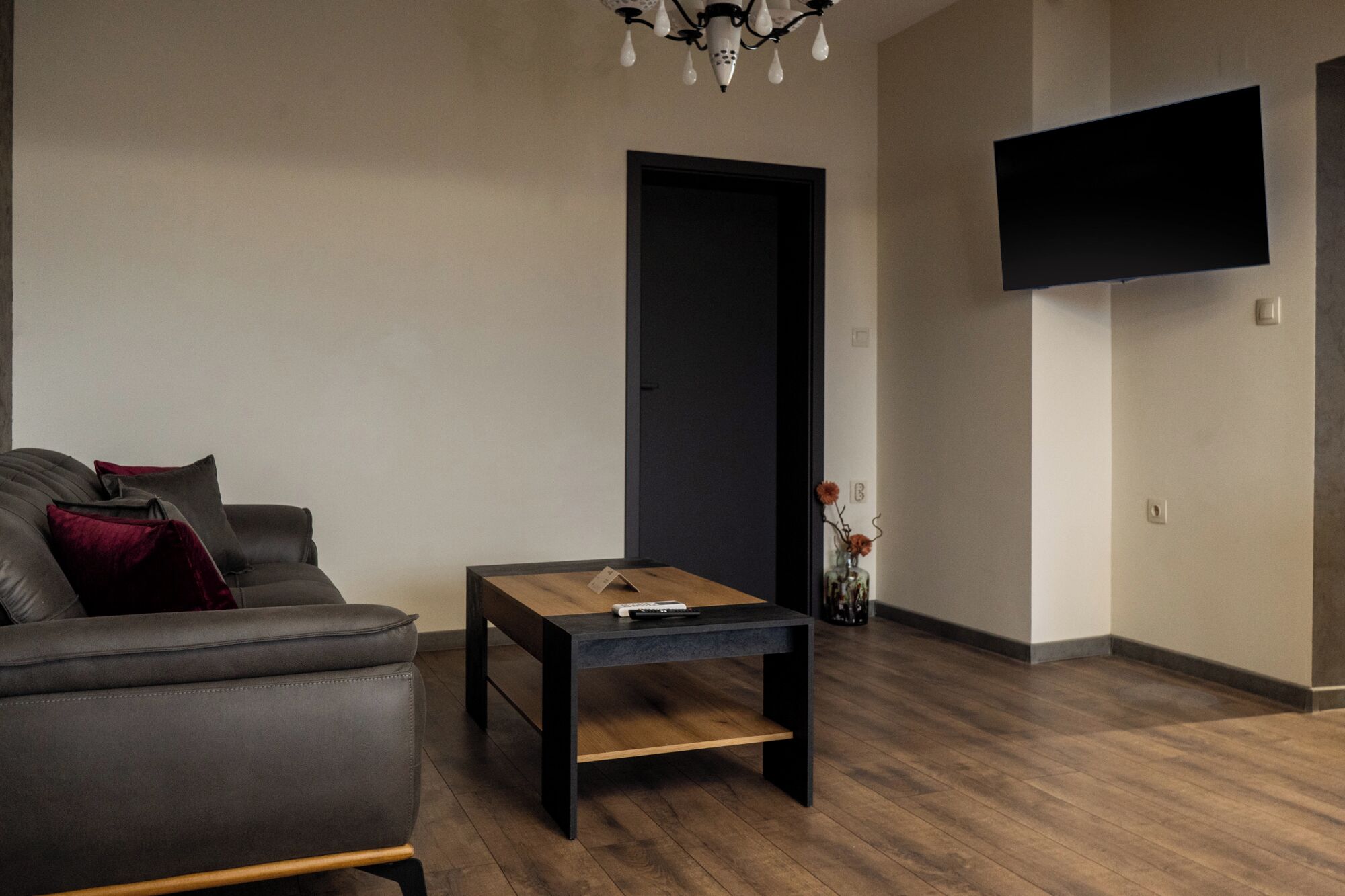 Una sala de estar moderna con un sofá de cuero oscuro, una mesa de centro de madera y un televisor de pantalla plana montado en la pared.