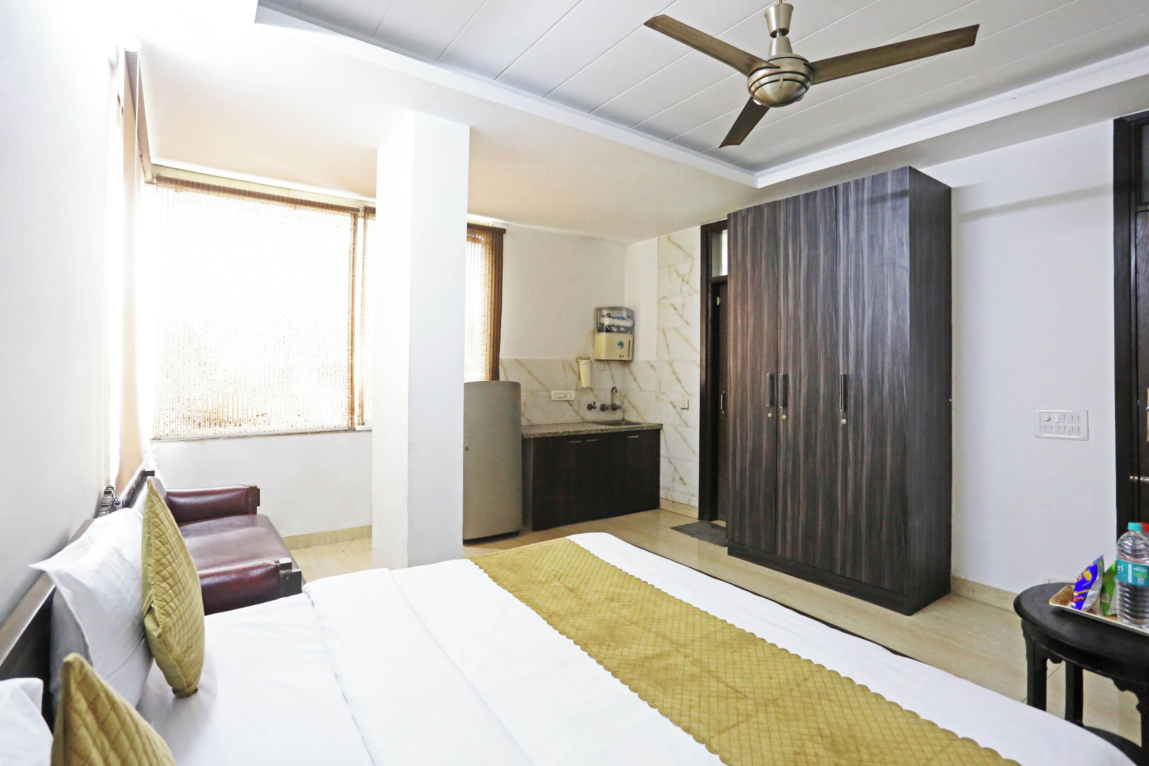 A hotel room with a bed, a desk, a wardrobe, a ceiling fan, and a window with curtains.