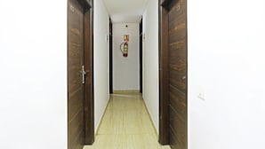 Un pasillo estrecho con puertas de madera a ambos lados, un extintor de incendios en la pared y un interruptor de luz en la pared derecha.