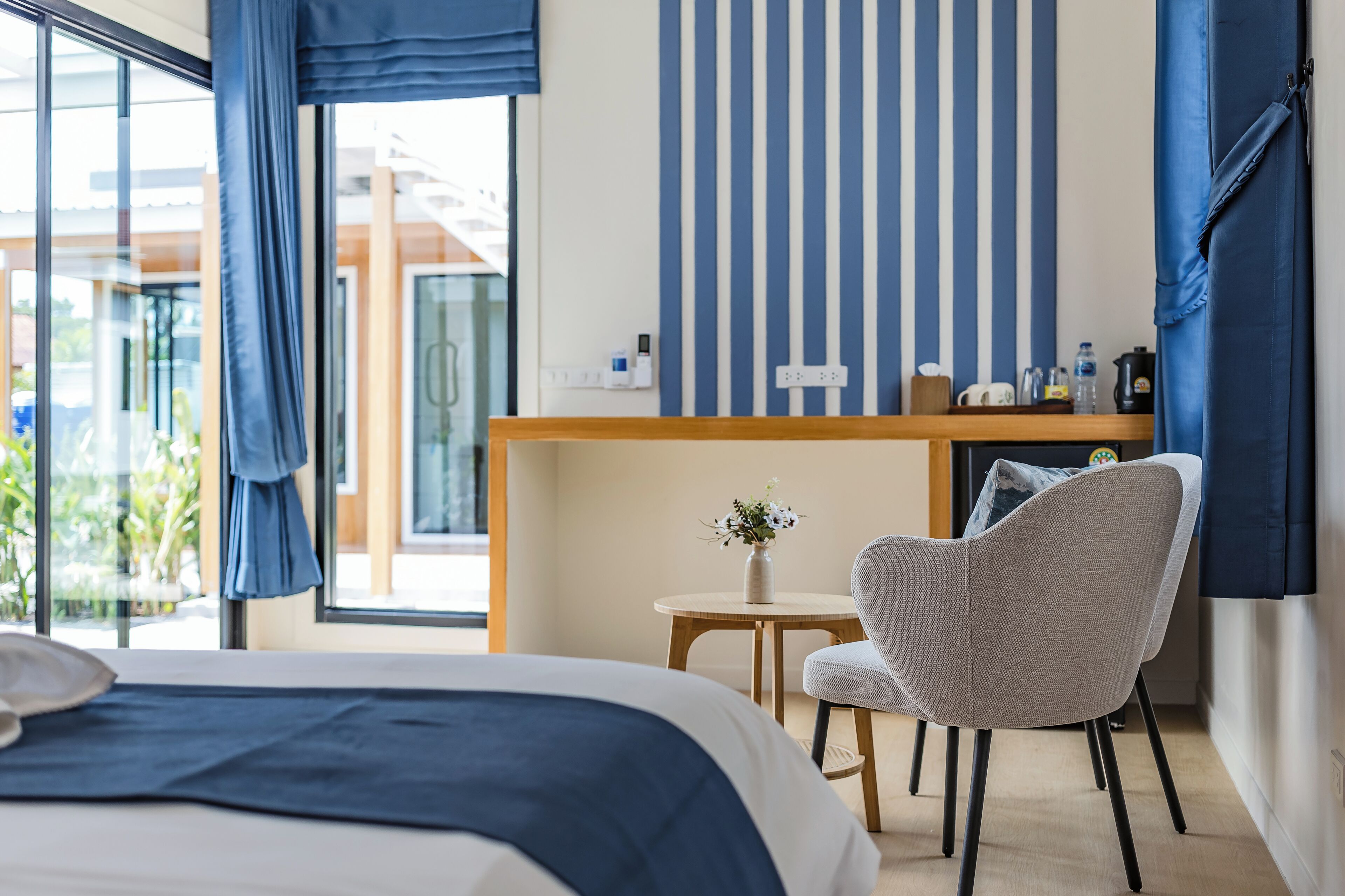 A hotel room with a bed, a desk, a chair, and a small table with a vase of flowers.